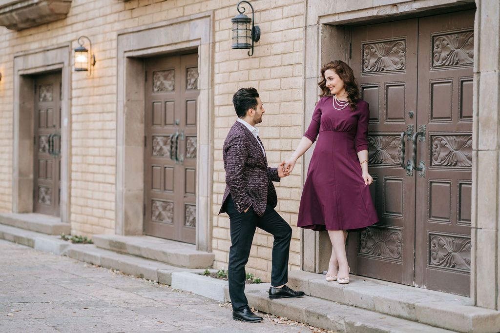 Couple in formal wear holding hands against ornate wooden doors.