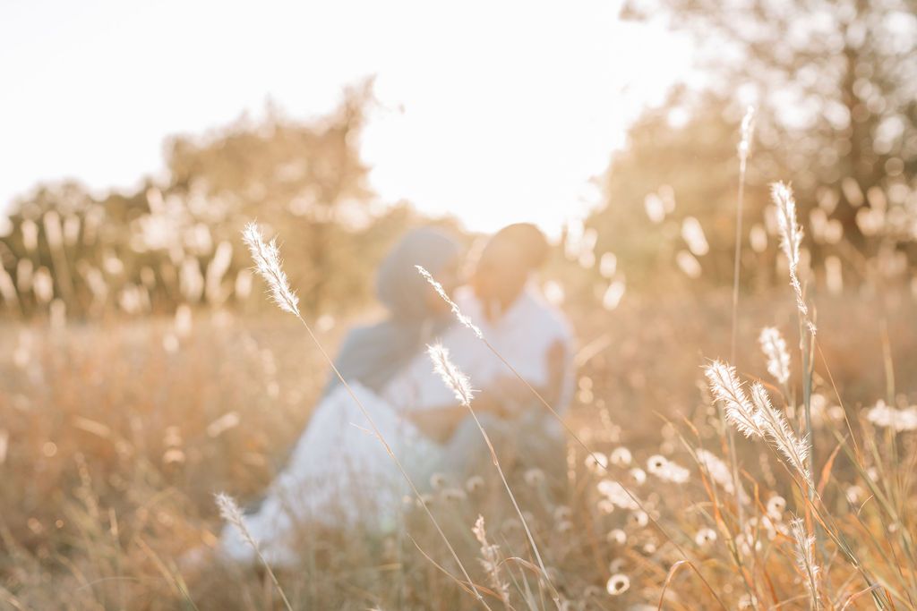 Dreamy backlit couple sitting in golden field at sunset.