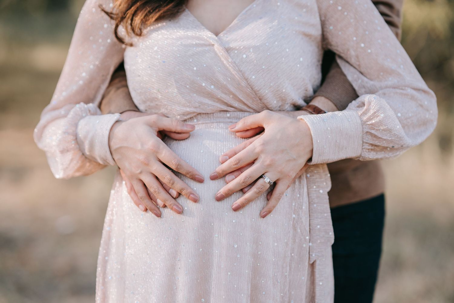Loving hands cradle a pregnant belly while wearing a delicate blush-colored dress.