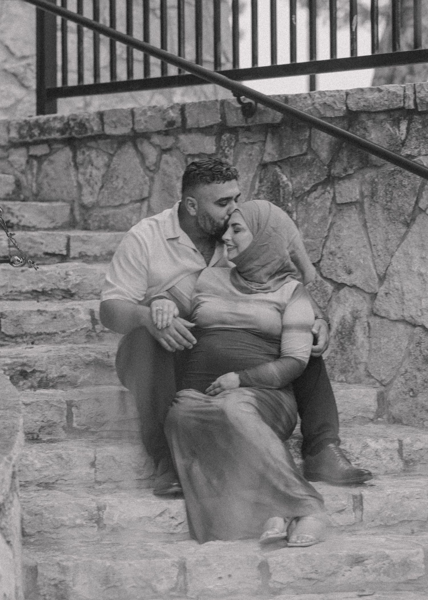 A couple sharing an intimate moment while sitting on stone steps in black and white.