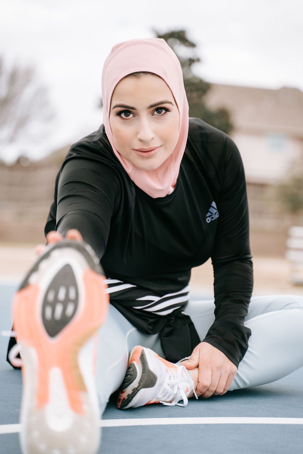 Athlete in hijab and workout gear stretches during exercise on outdoor court.