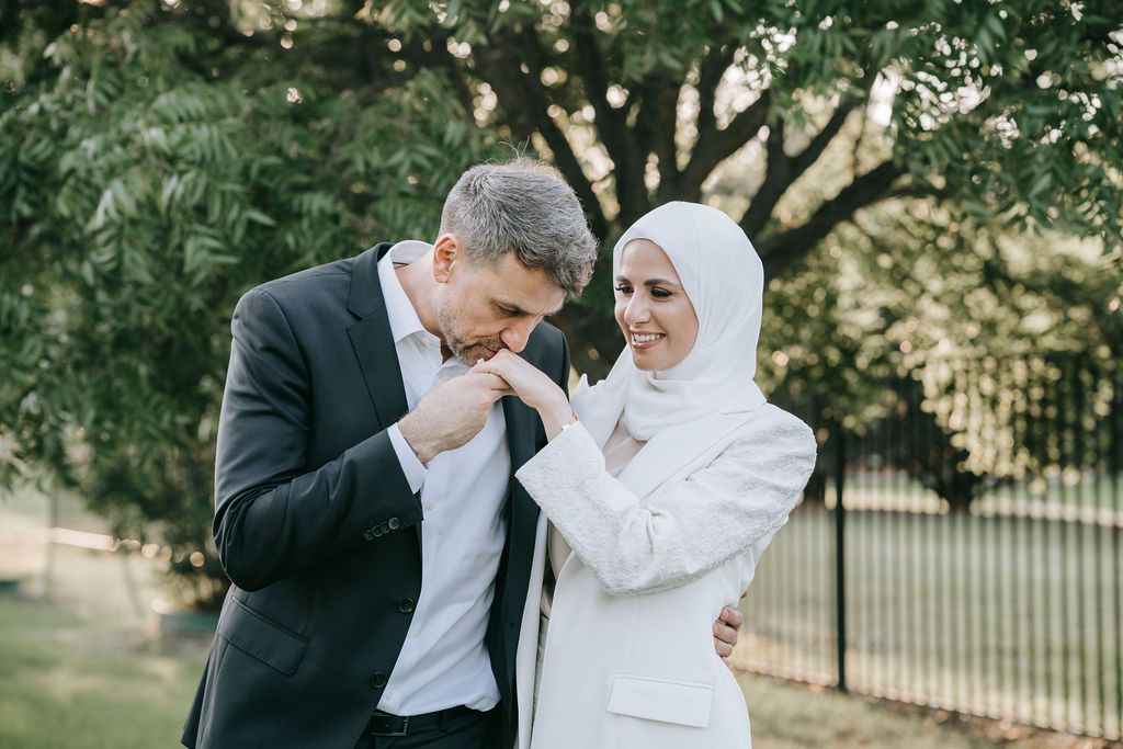 Couple sharing a tender moment outdoors near a fence and trees.