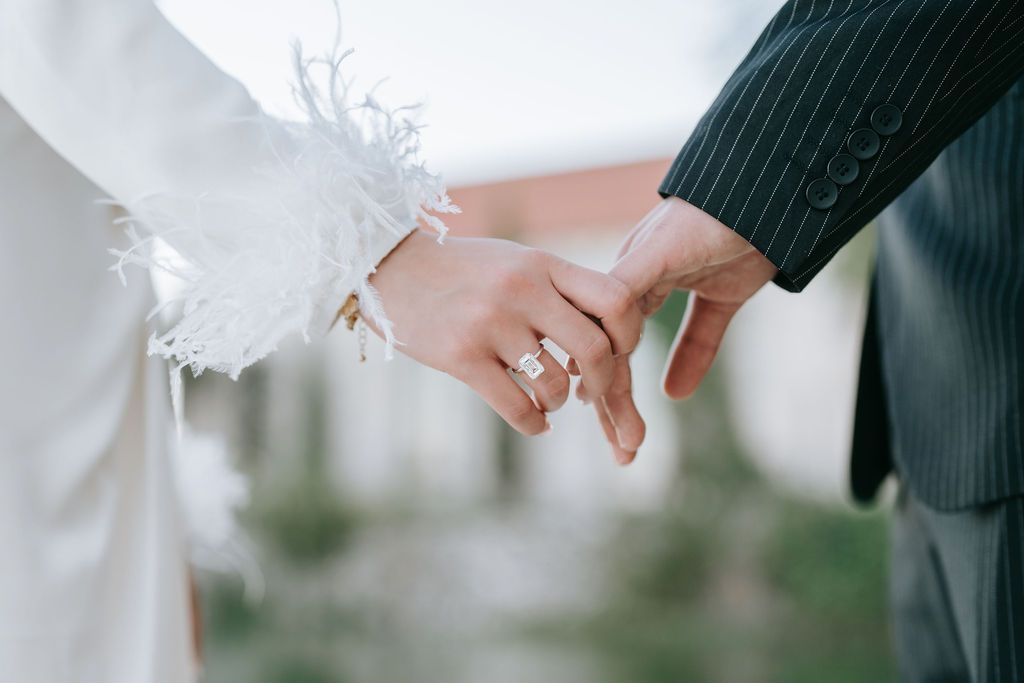 Close-up of two hands joined together, with delicate lace from a wedding dress visible.