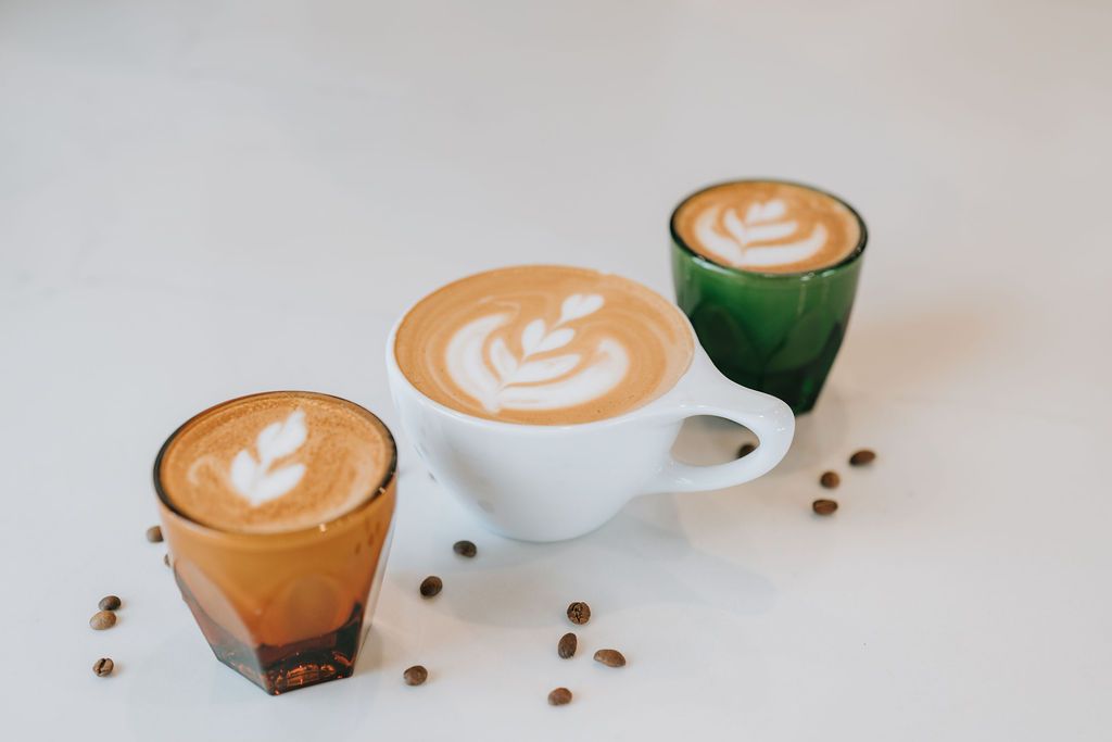 Three artisanal coffee drinks with latte art displayed on white surface.