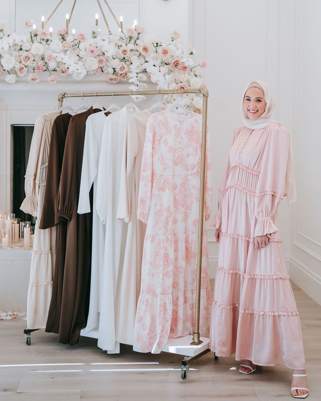 Modest fashion display with pink and neutral dresses on rack beneath floral chandelier.