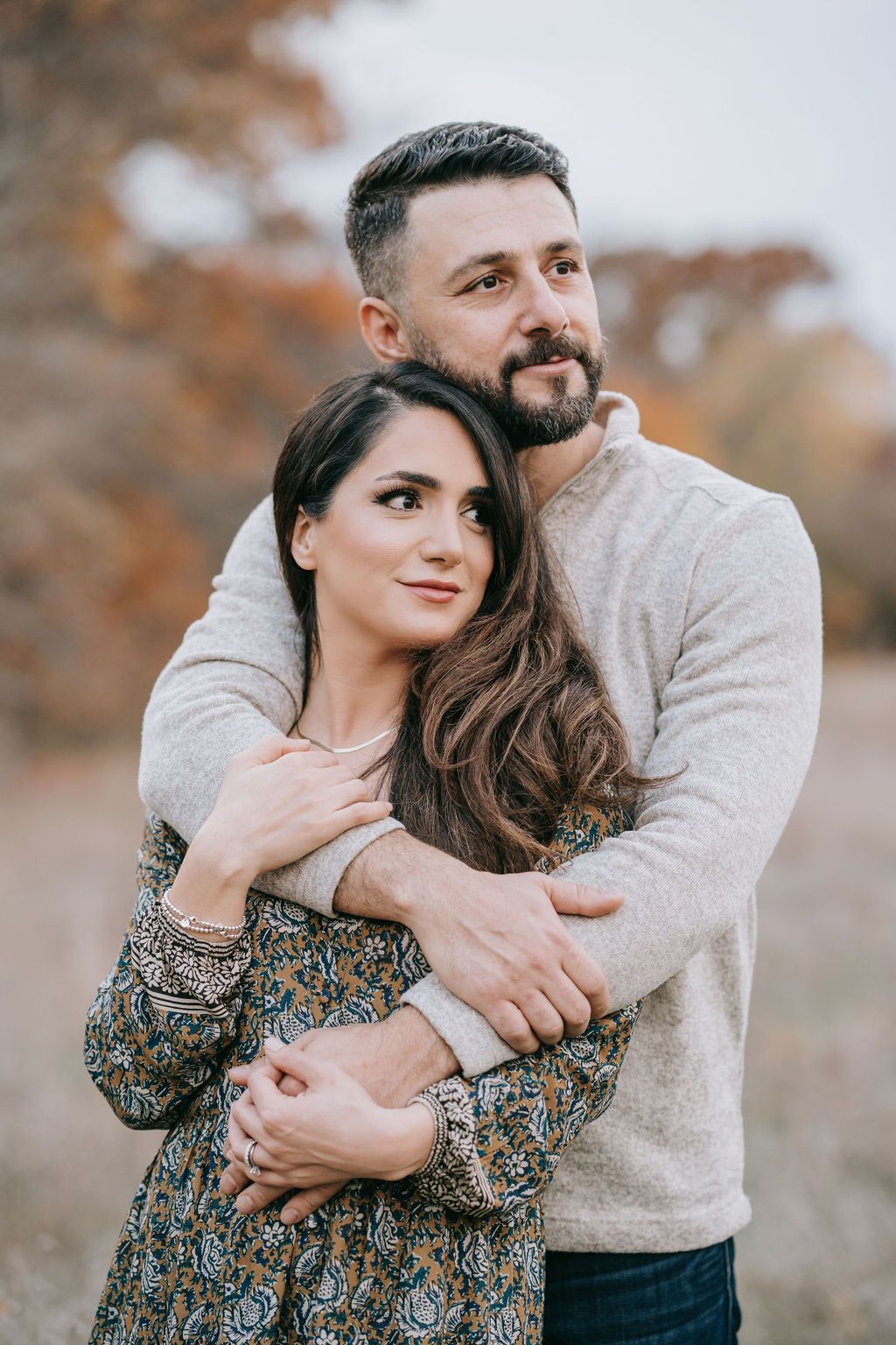 Couple in casual sweater and floral dress sharing intimate embrace in natural setting.