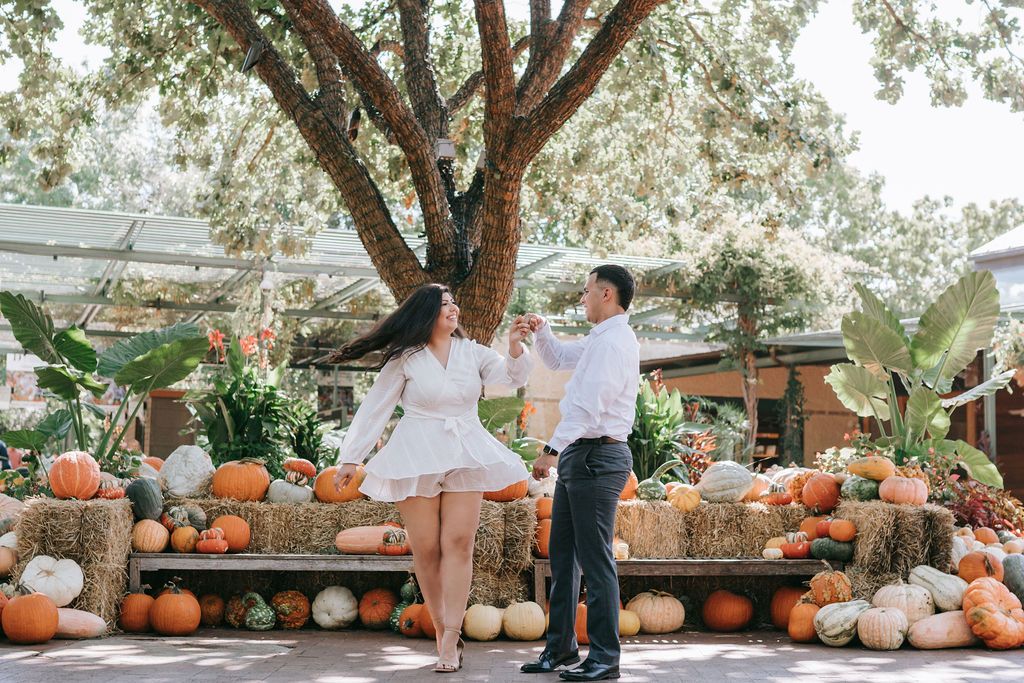 Couple dancing among pumpkin display in garden setting.