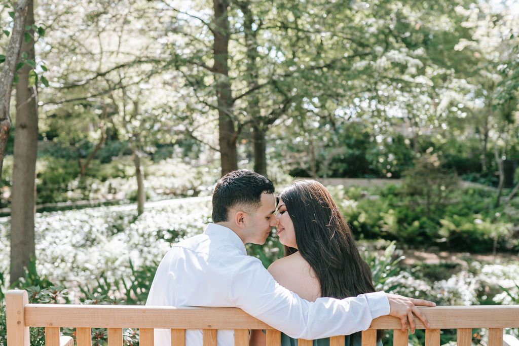 A couple shares an intimate moment while sitting together on a wooden bench in a spring garden.