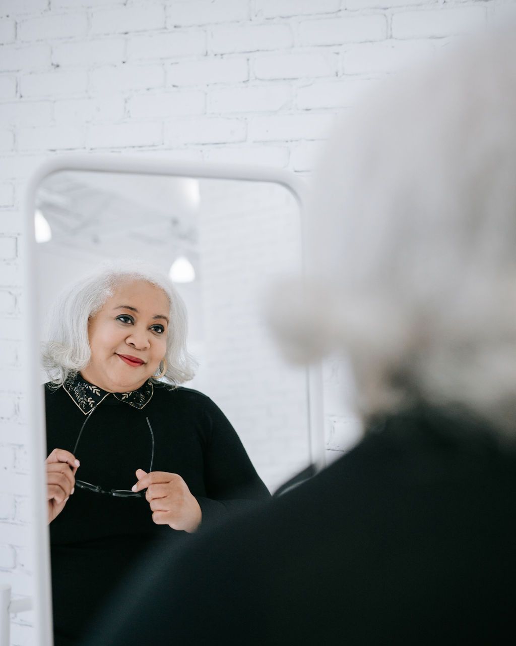 Person with silver hair looking in mirror wearing black outfit.
