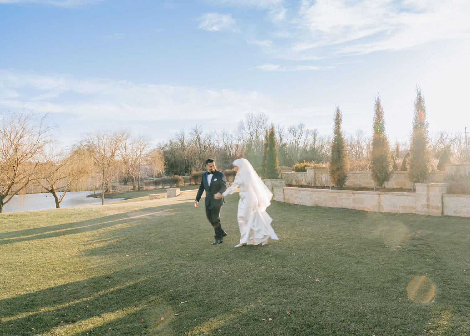A couple dancing together on a grassy lawn with cypress trees and blue sky in the background.