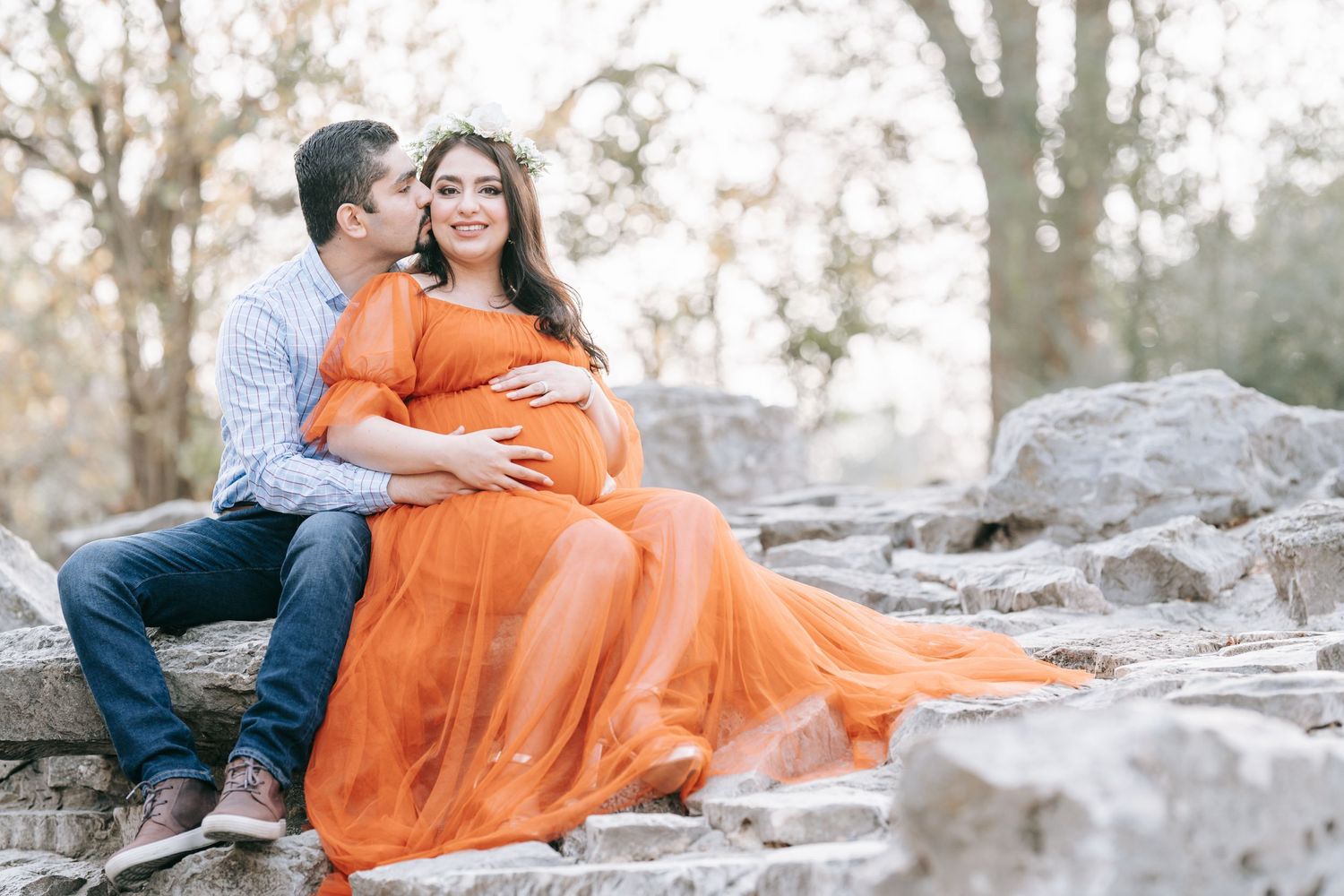 A maternity photo featuring a flowing orange dress on rocky natural terrain.