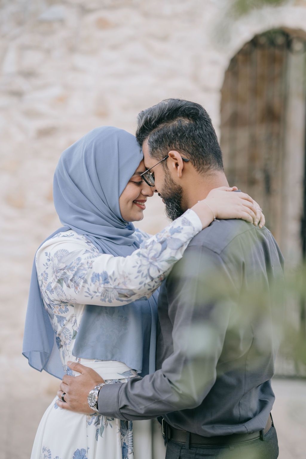 Muslim couple in an intimate embrace shares a tender moment against a stone wall.
