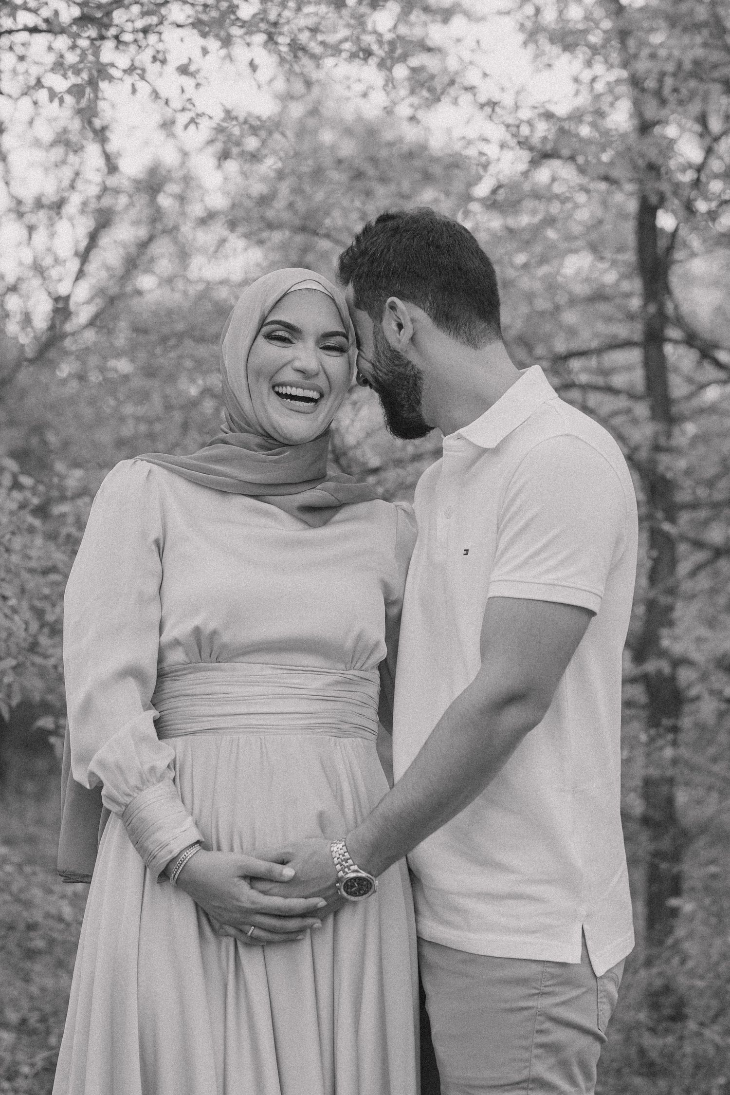 A couple shares a joyful moment together outdoors during a pregnancy photoshoot.