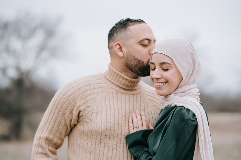 Romantic couple embracing outdoors, wearing cozy sweaters with hijab style in muted tones.
