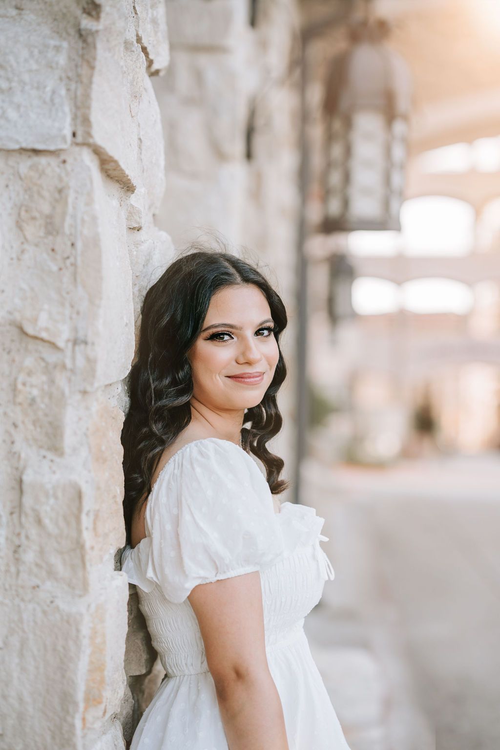 Portrait against stone wall wearing white dress with puff sleeves.