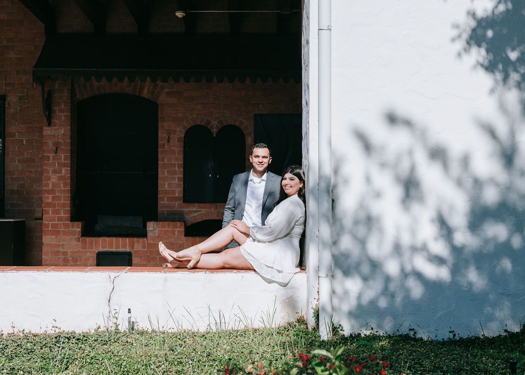 Couple sitting casually on white ledge of brick building.