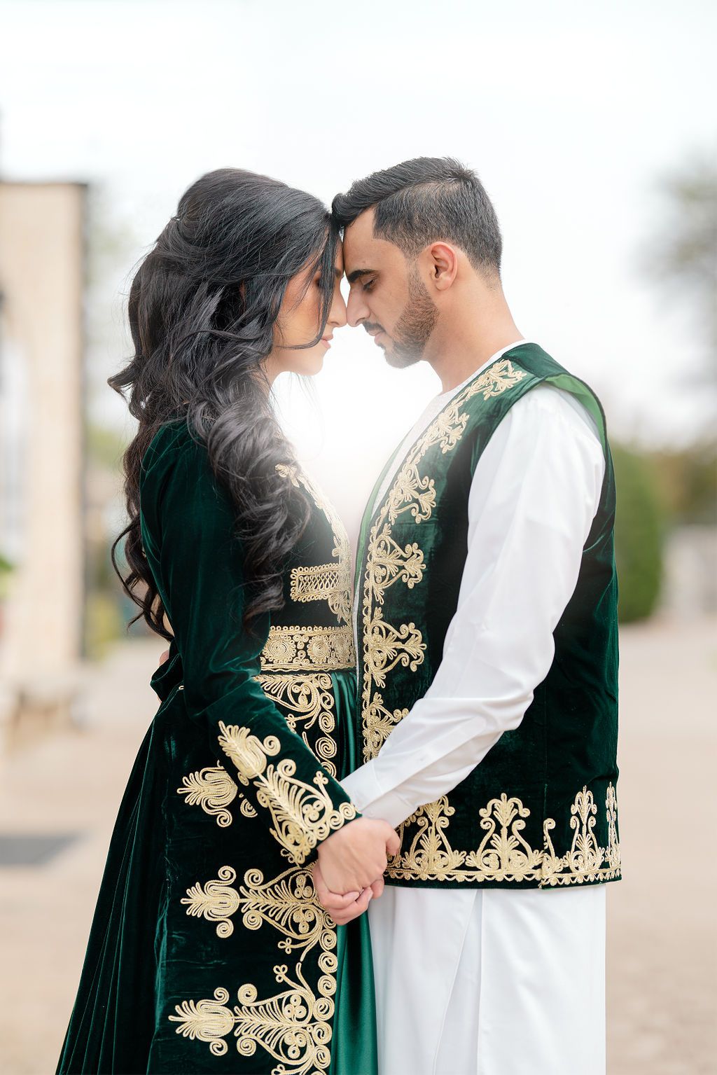 Couple in elegant emerald velvet attire with gold embroidery standing close together.