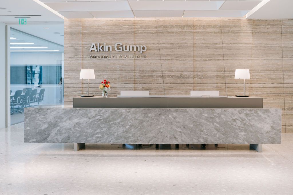 Modern office reception desk with Atkin Gump signage and marble finishes in a minimalist corporate setting.