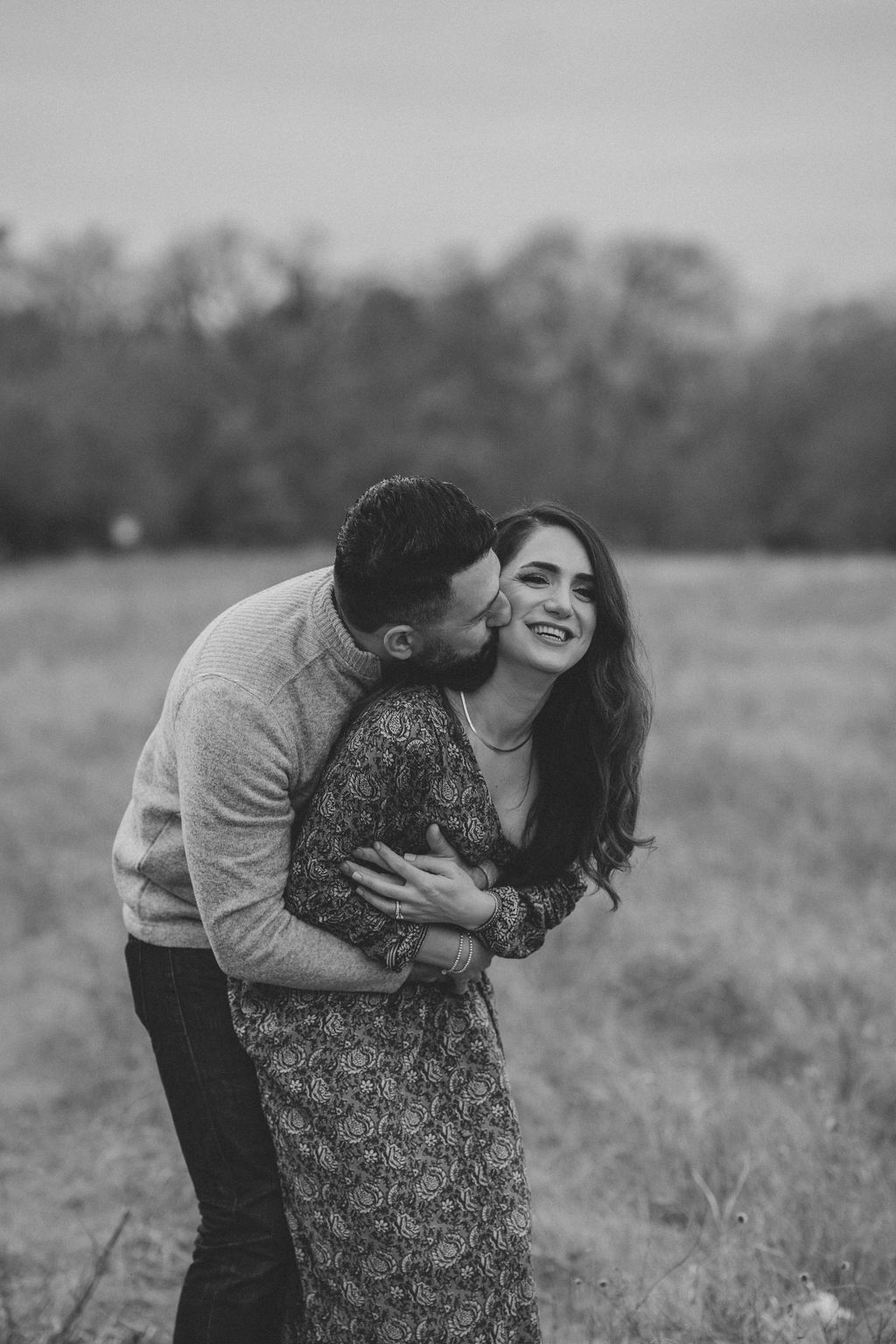 Black and white portrait of couple laughing and embracing in field with natural backdrop.