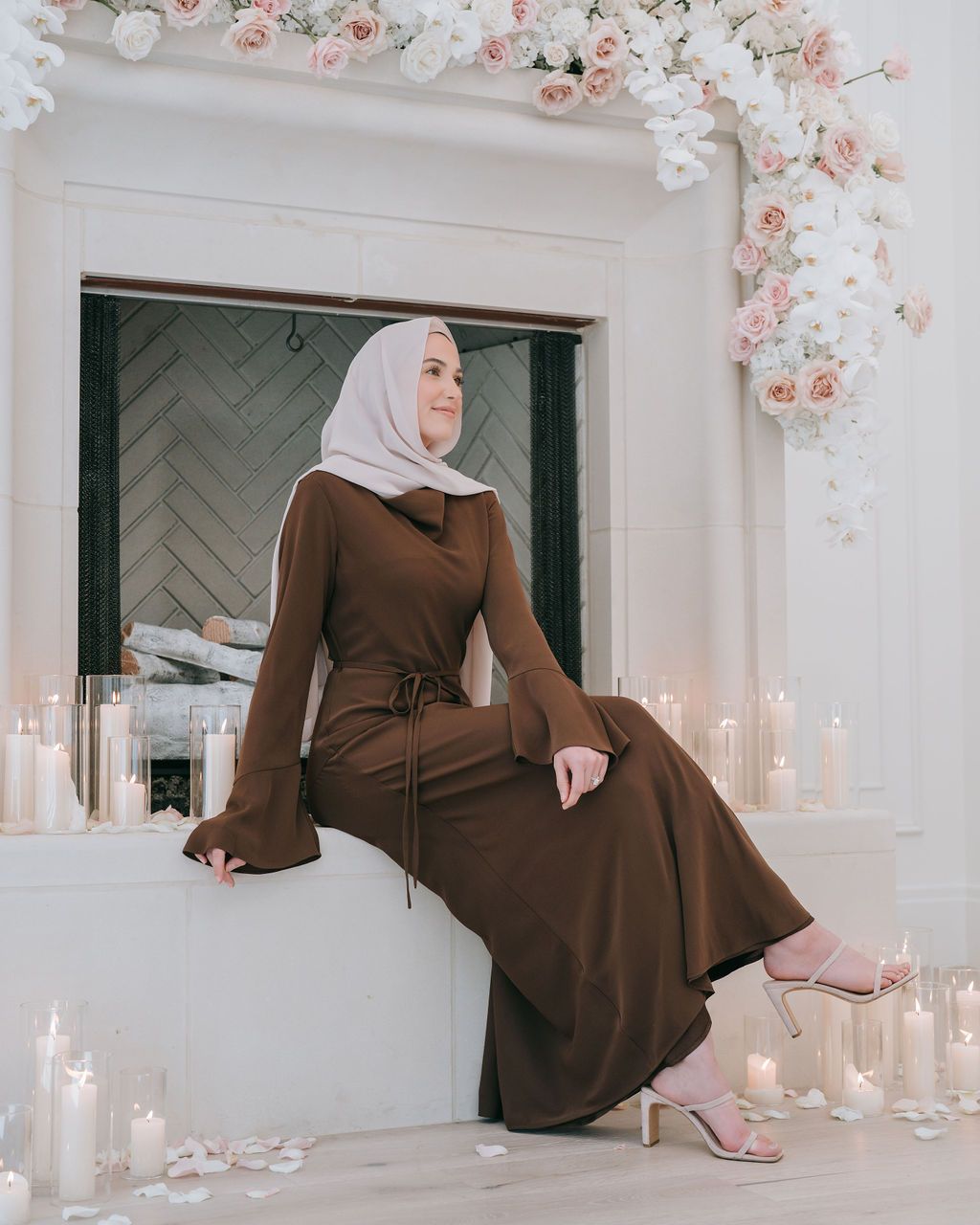 Brown modest dress photographed in elegant setting with floral decorations and candles.