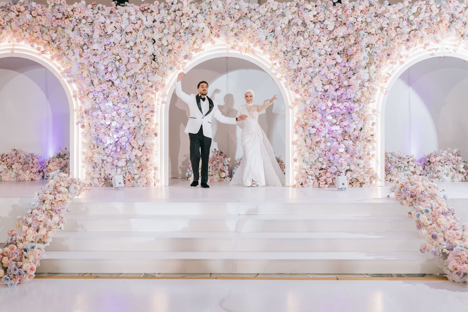 Elegant wedding ceremony setup with arched floral doorways and white steps decorated in soft pink and white blooms.