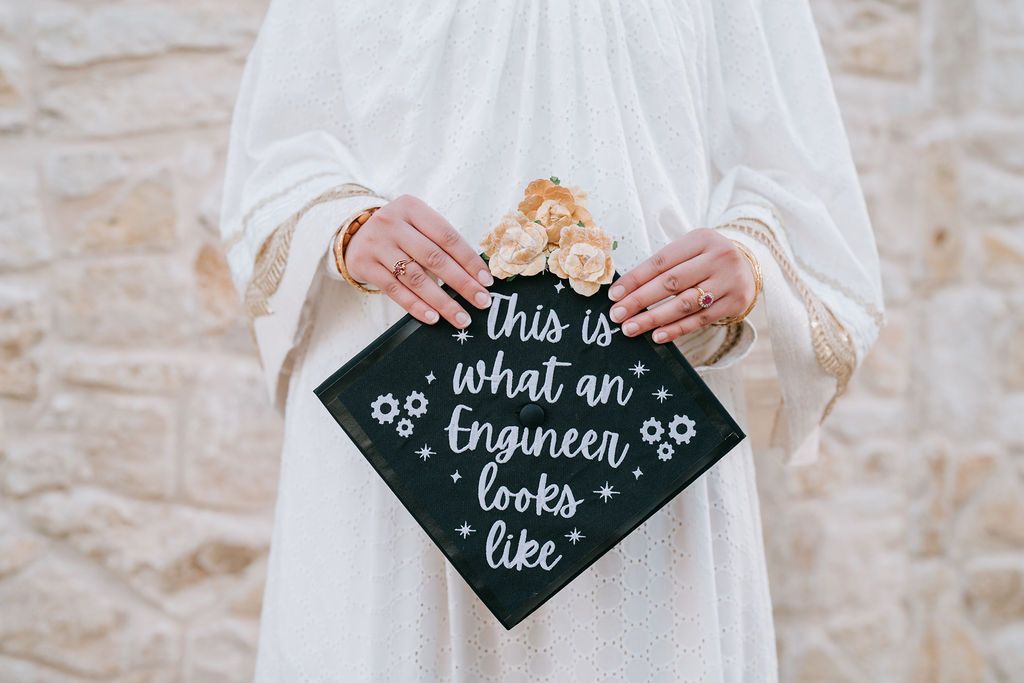 Decorated graduation cap with handwritten quote held against stone background.