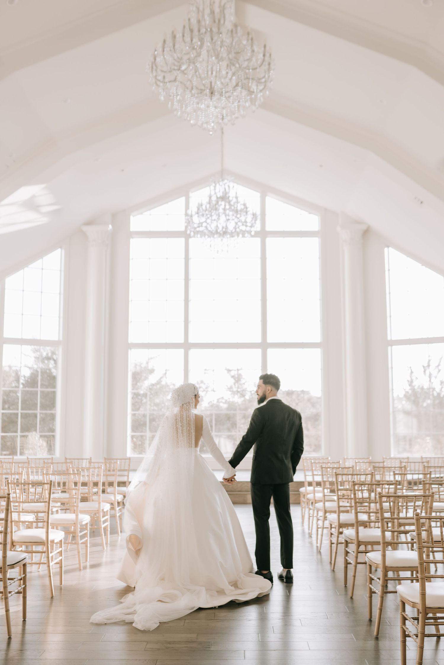 Bride and groom walking down aisle in grand wedding venue with large chandelier in Dallas.
