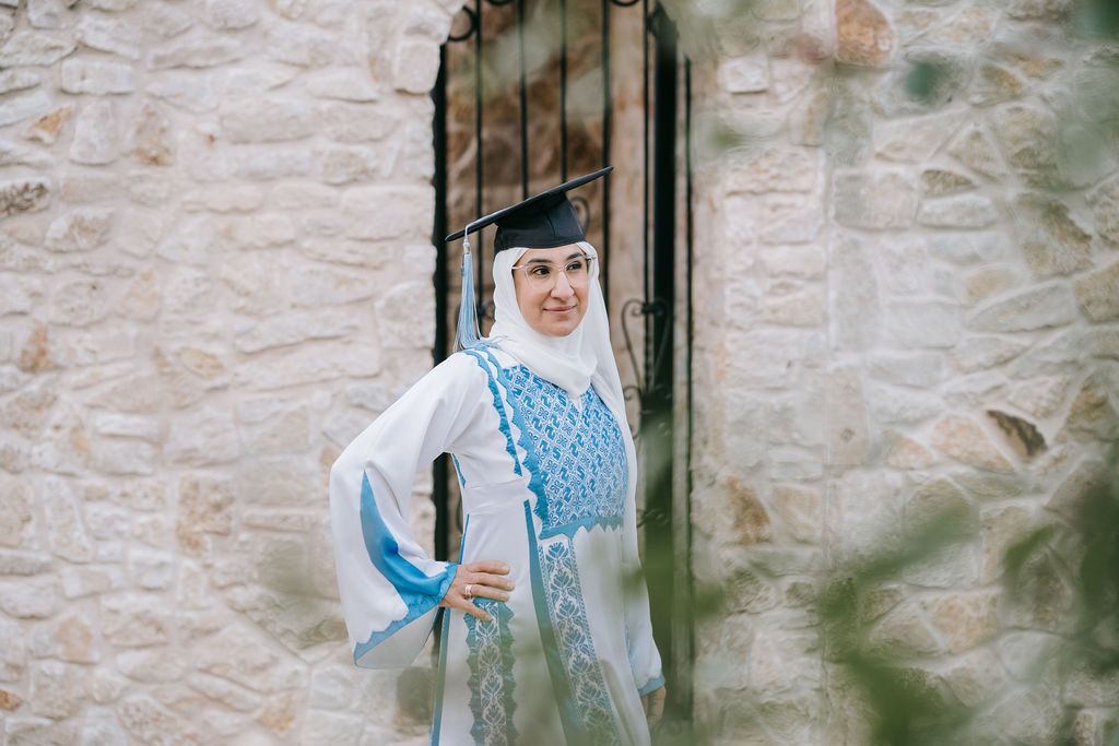 Graduate in blue and white traditional dress poses confidently by stone doorway.