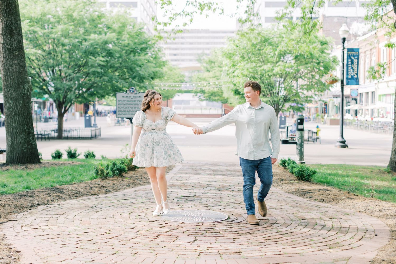 A couple holds hands and walks together on a brick path in a lush urban park on a sunny day.