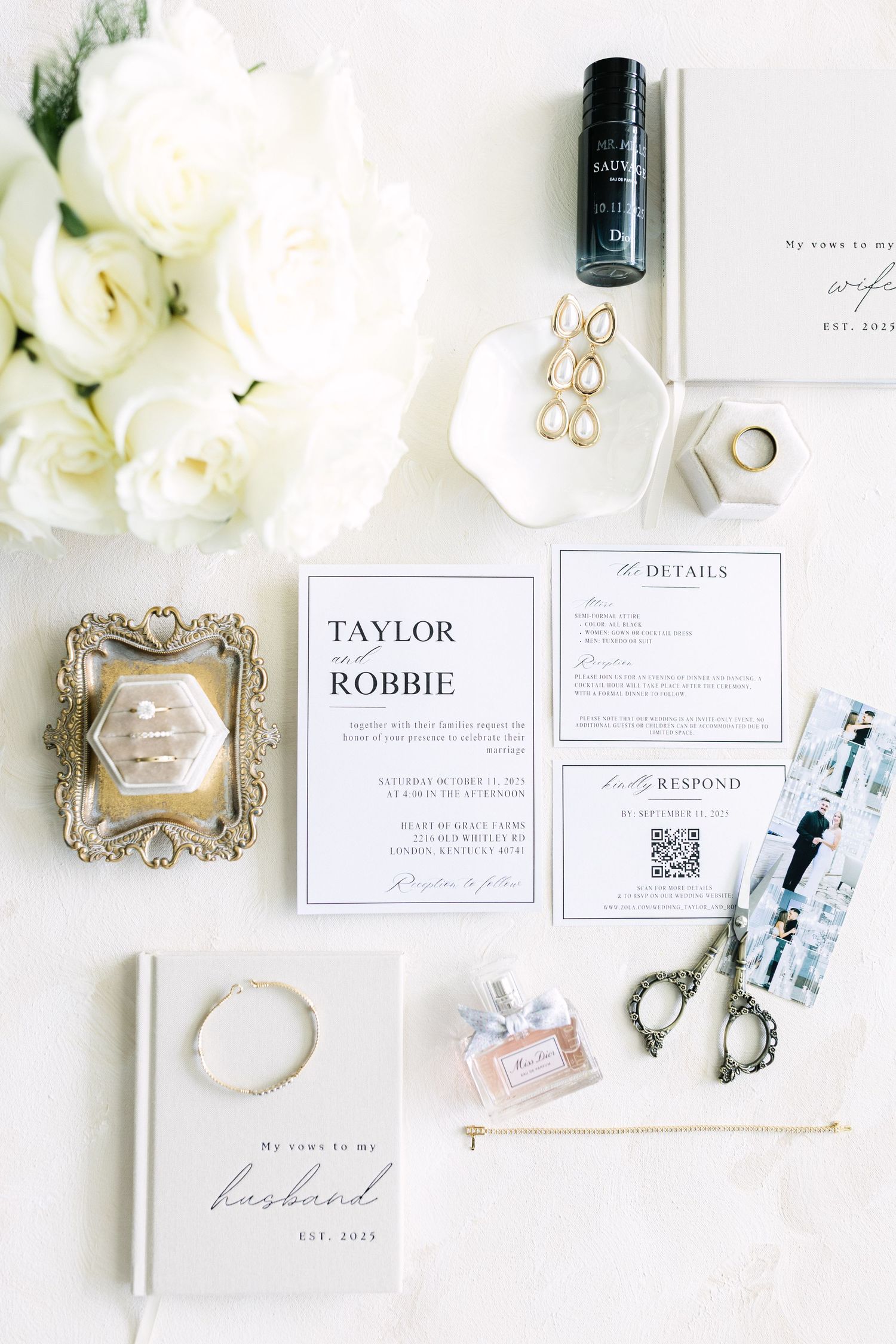 Elegant wedding invitation suite for Taylor and Robbie displayed with white roses, perfume, gold earrings, and bridal accessories.