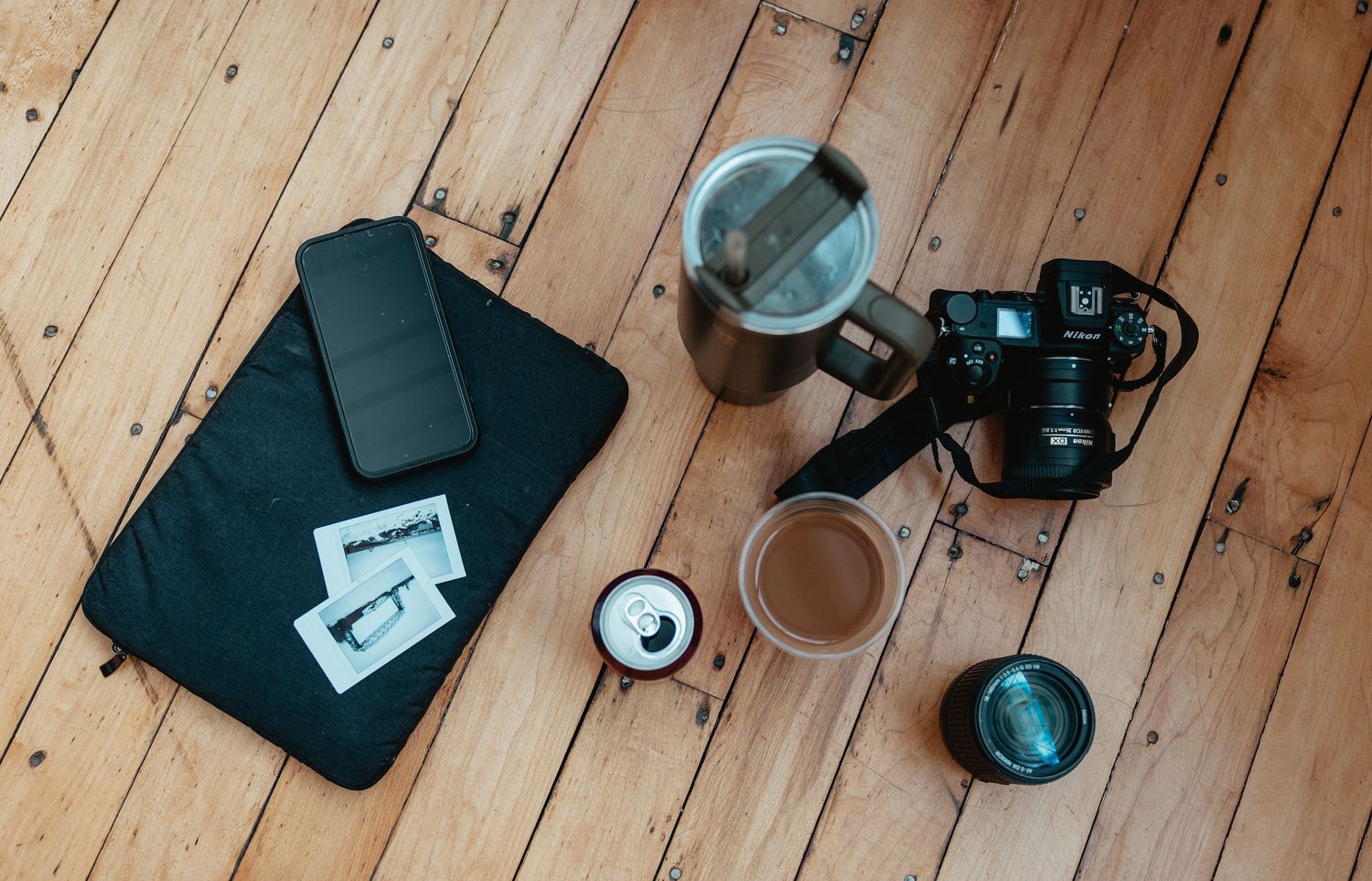 Flatlay of photography gear including camera, laptop and coffee on wooden floor.