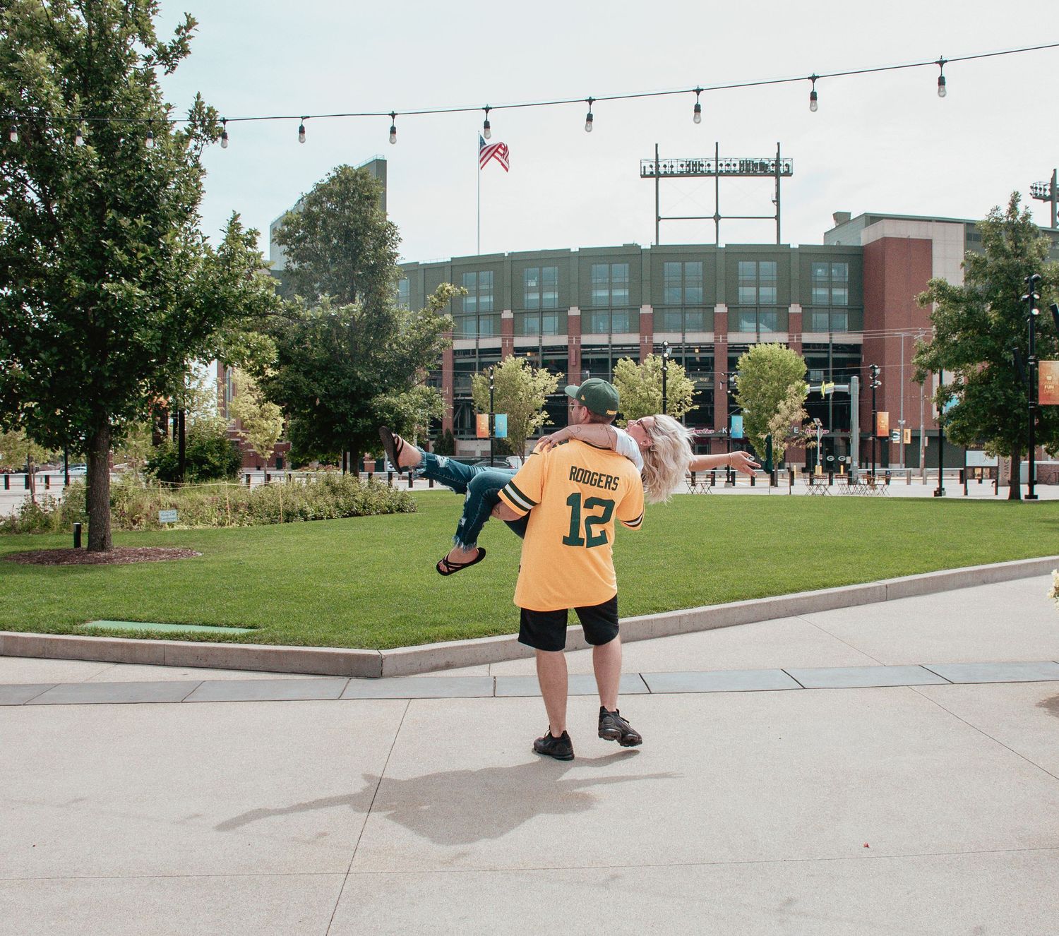 Sports fan in yellow jersey walking outside stadium with string lights overhead.