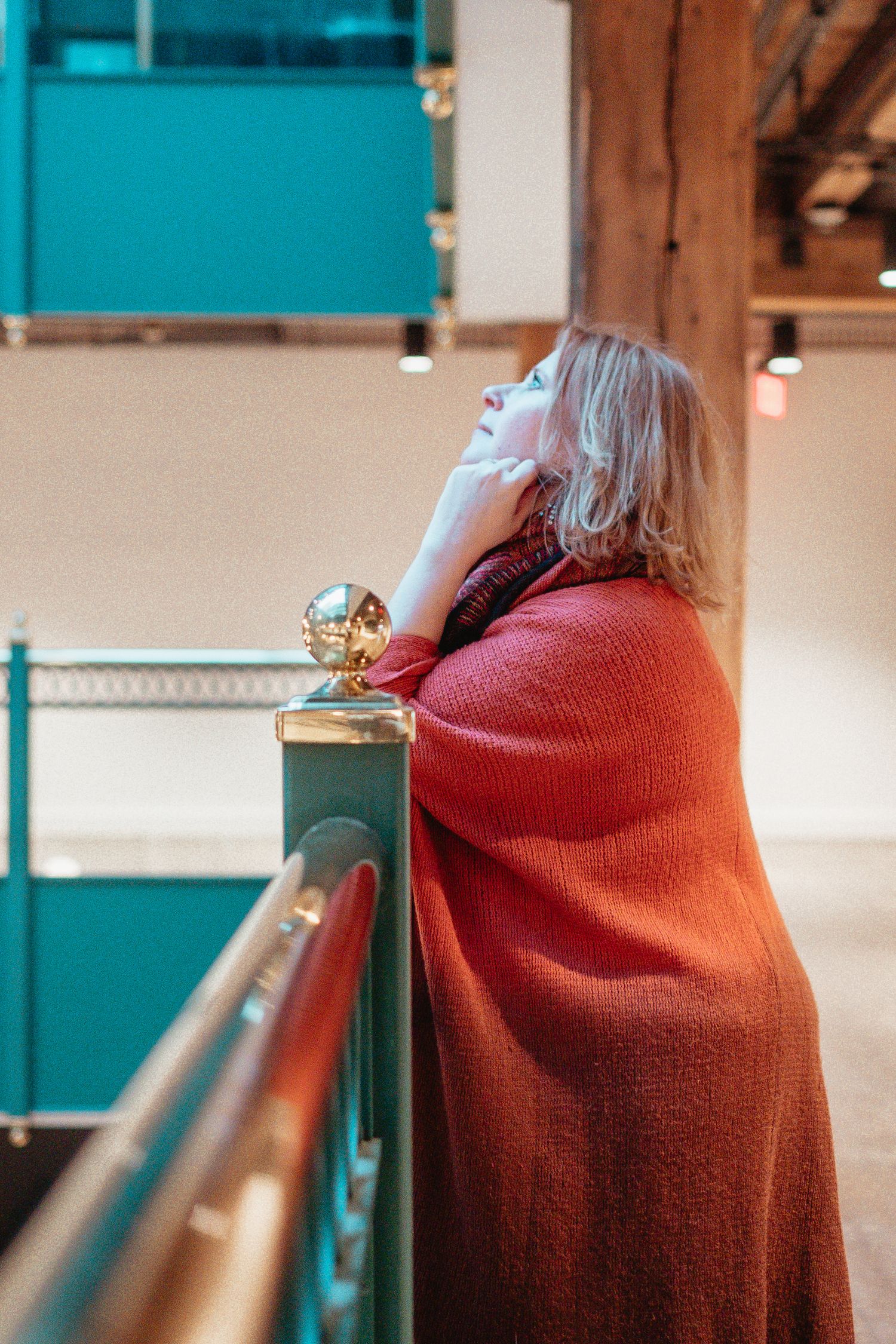 Person in red sweater leaning on railing in modern industrial space.