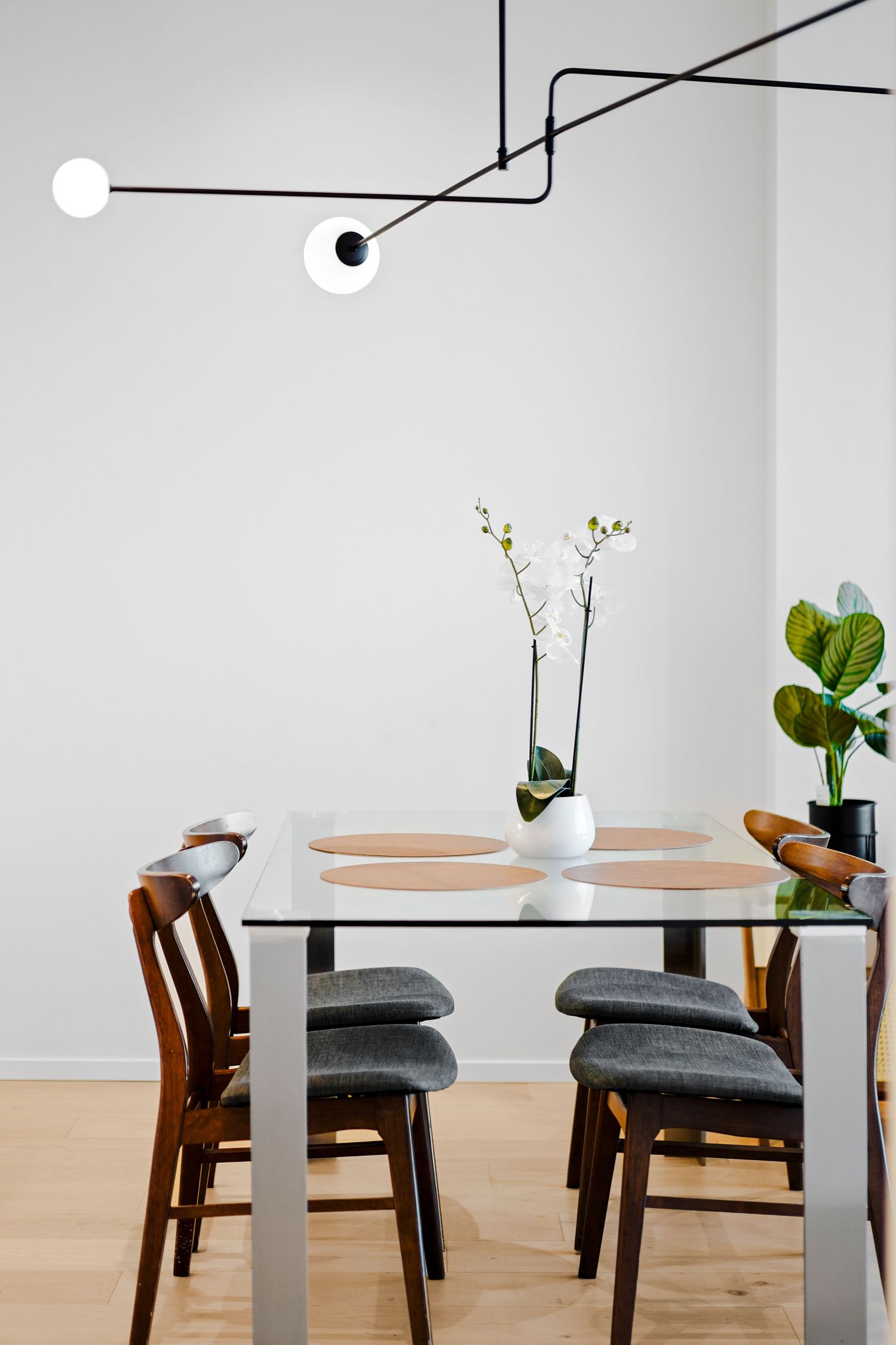 Modern dining area with geometric black pendant light, wooden chairs, and potted orchid centerpiece.