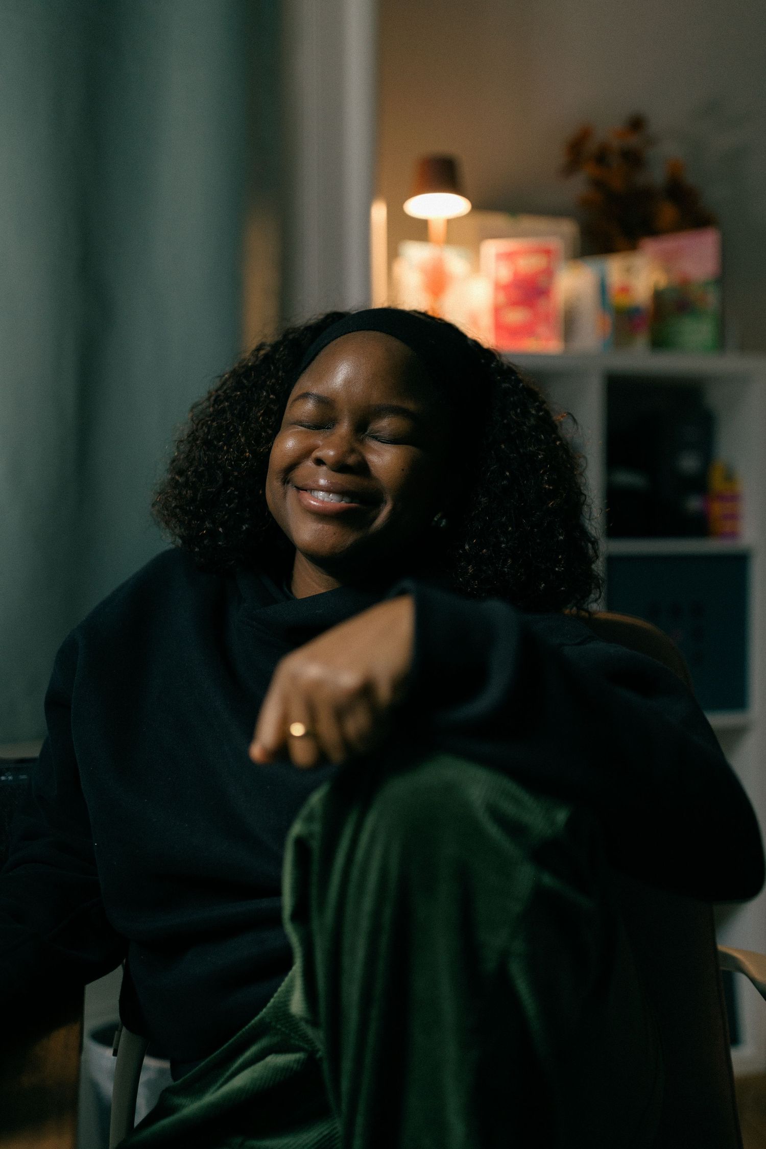 Person in dark clothing smiling and laughing in a dimly lit room with warm ambient lighting.