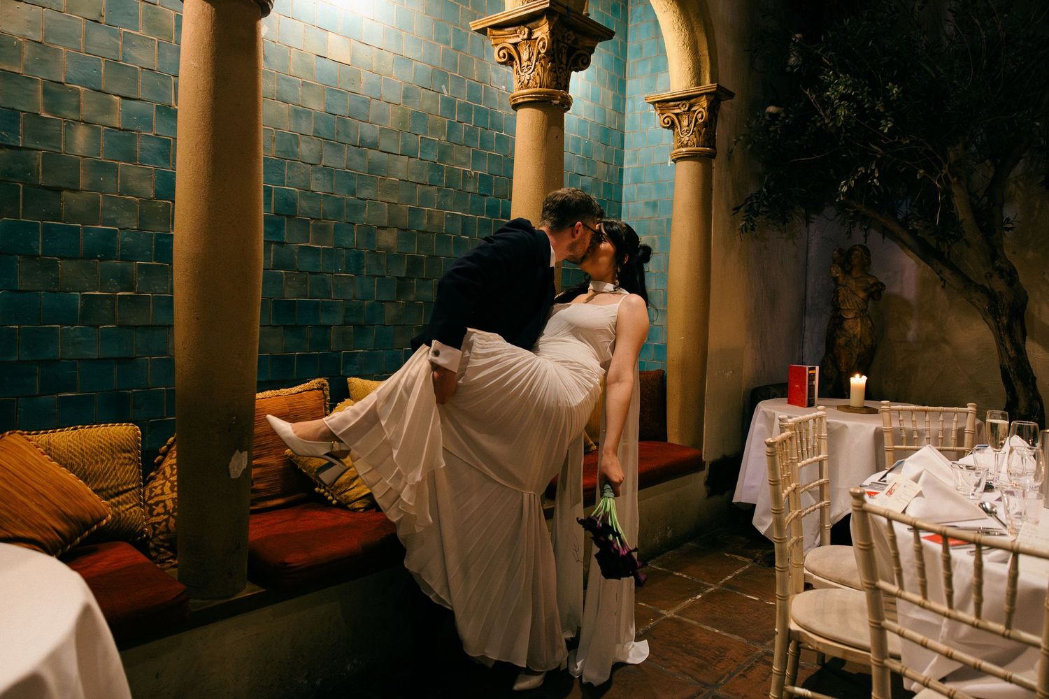A series of romantic wedding photos showing a couple in white attire posing in an elegant columned venue at night.