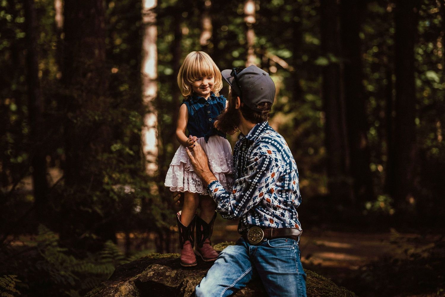 A cowboy father and his daughter smiling in a candid portrait located in a forest in Campbell River.
