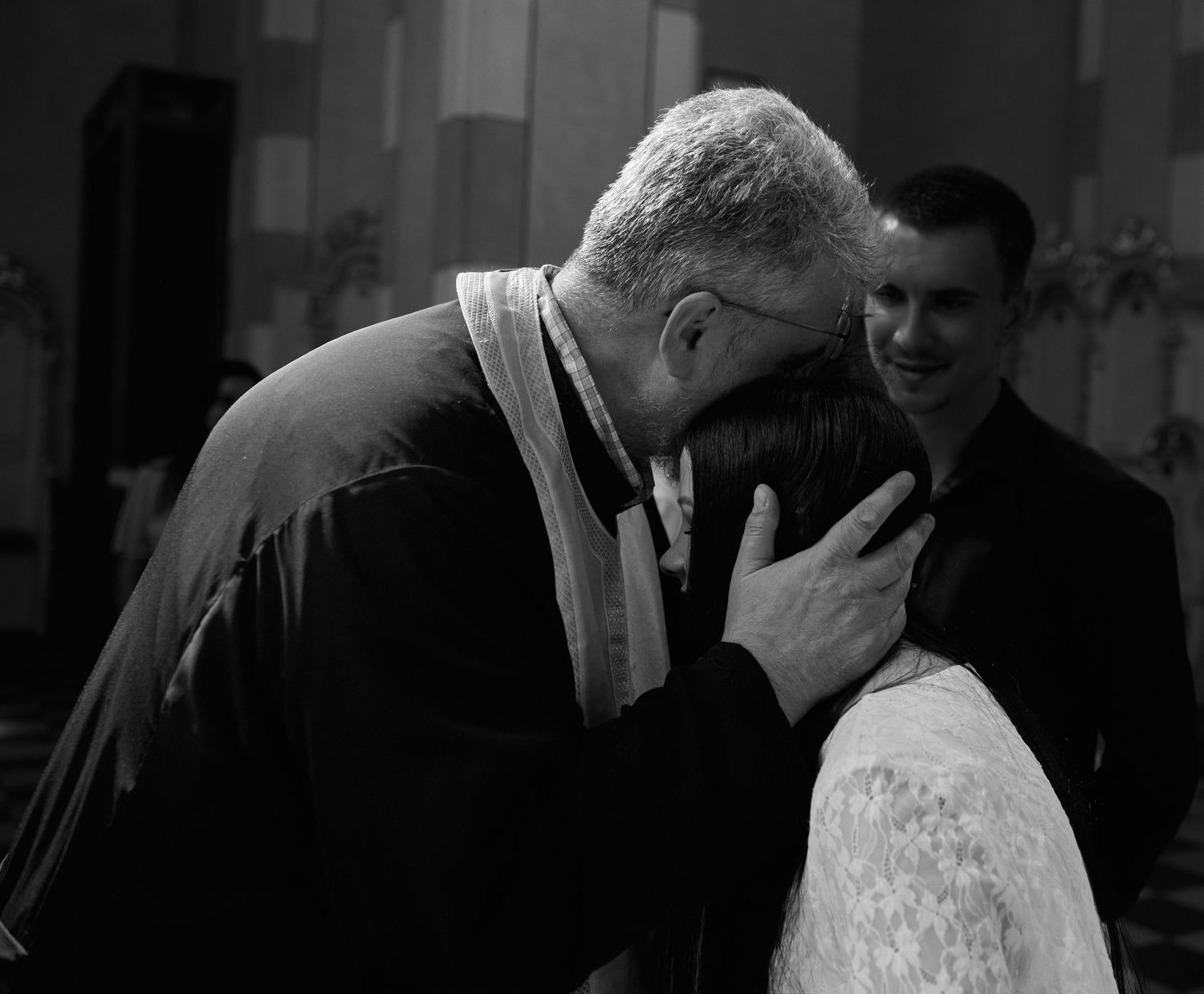 Moment intim alb-negru între preot și mireasă în timpul cununiei religioase.