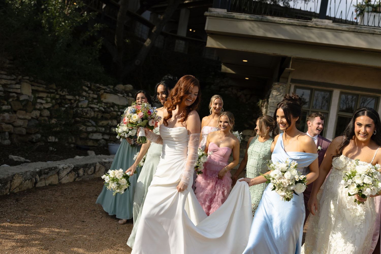 Bride with red hair and bridesmaids in pastel blue dresses walking with bouquets at outdoor wedding venue.