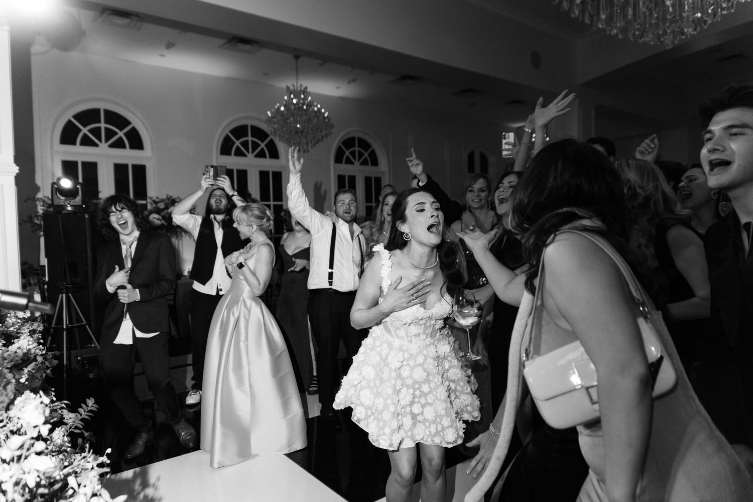 Black and white photo of wedding guests laughing and dancing joyfully at a elegant indoor wedding reception.