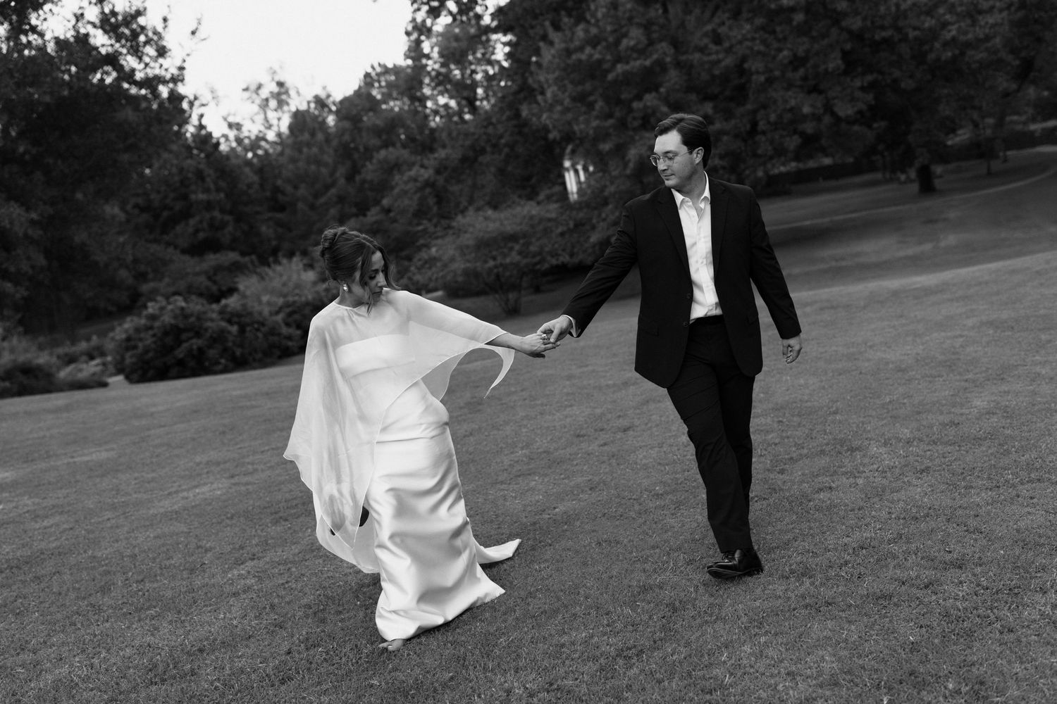 Black and white photo of a bride and groom dancing and holding hands on a lush green lawn.