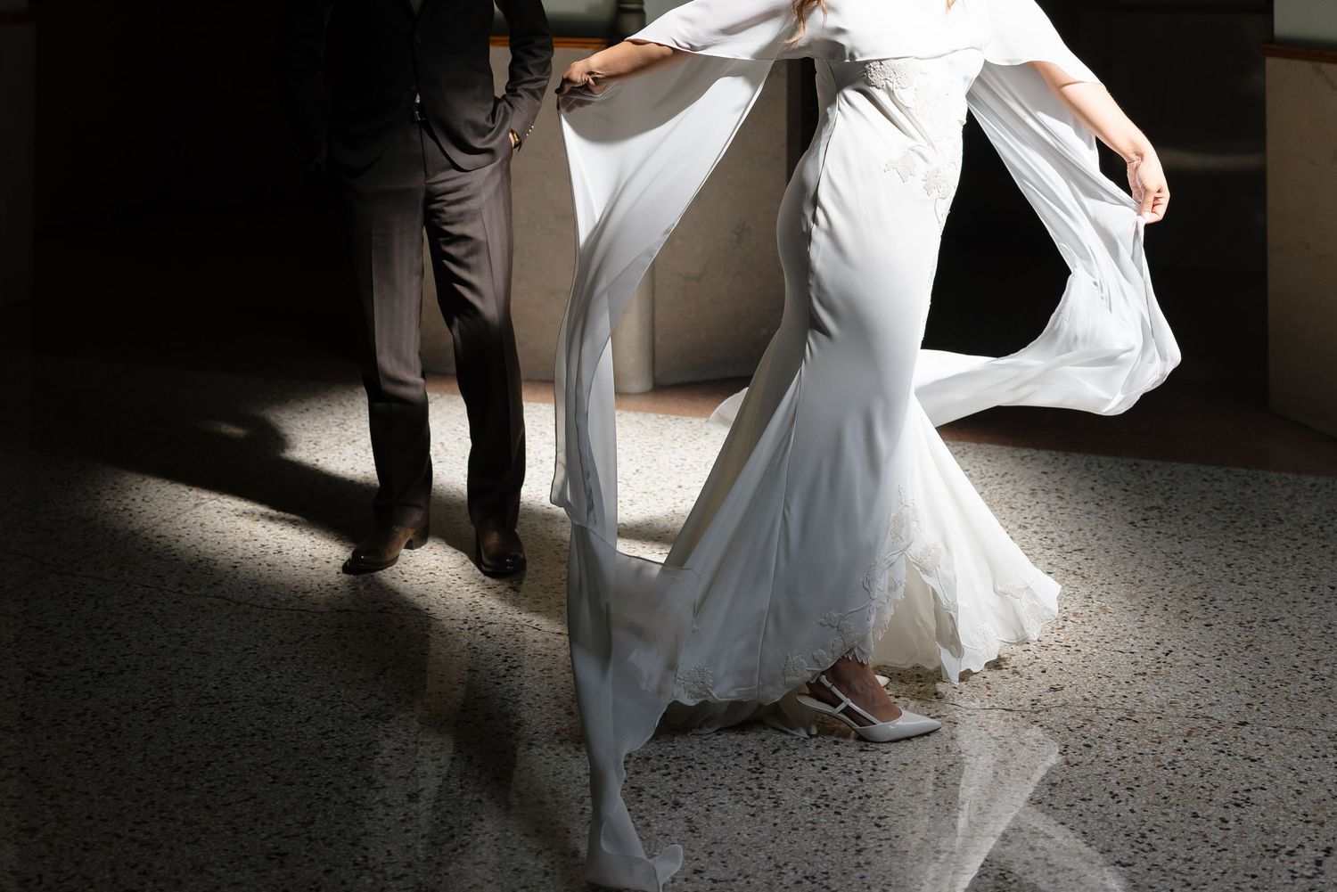 Bride in mermaid wedding gown with flowing veil poses in dramatic light and shadow.