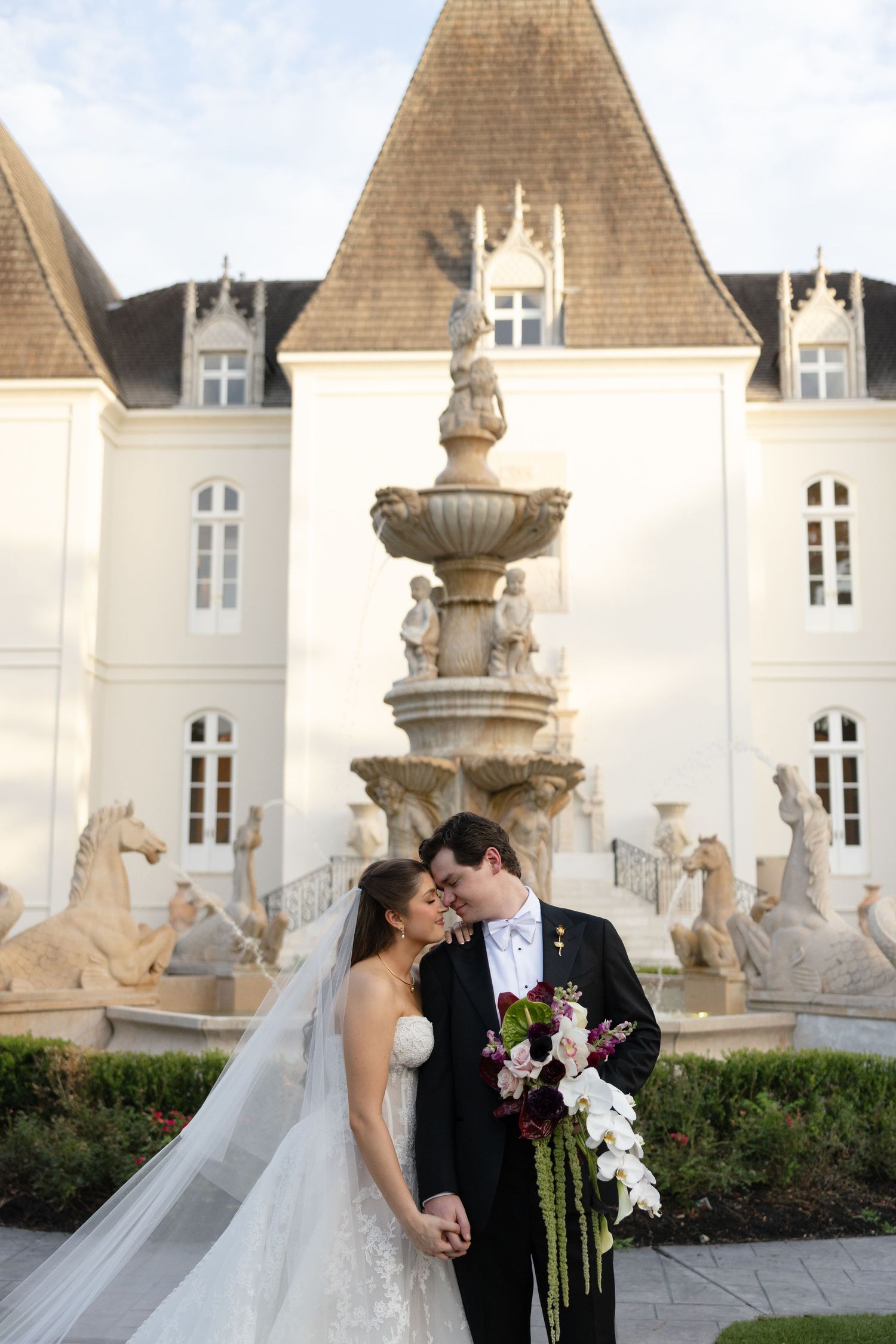 Bride and groom share romantic moment before ornate fountain at chateau wedding venue.