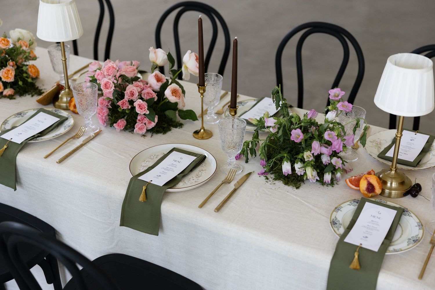 Elegant wedding reception tablescape with pink and lavender florals, gold candles, and sage green napkins.