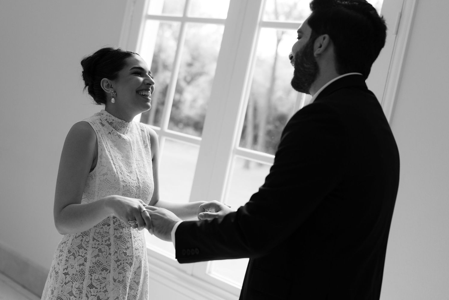 Black and white photo of bride and groom holding hands during intimate first look moment.