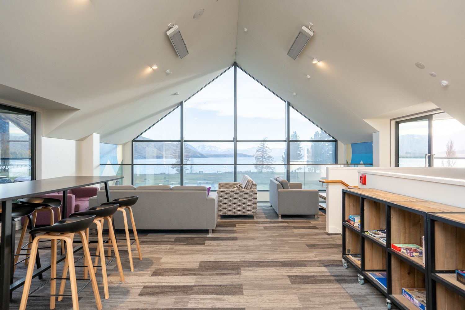 Bright A-frame lounge with floor-to-ceiling windows overlooking a lake, featuring modern furnishings.