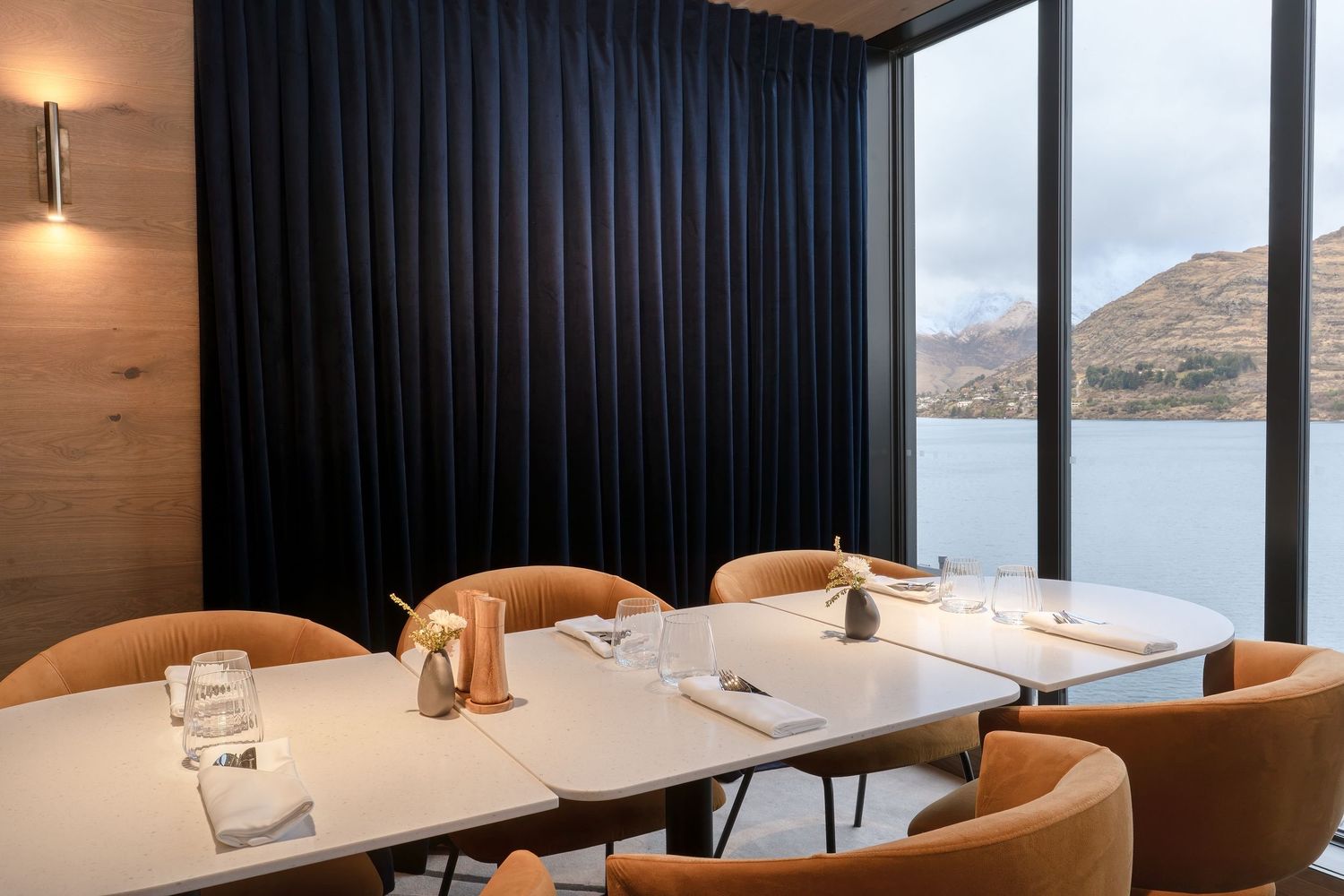 Elegant restaurant dining table with amber chairs and panoramic lake and mountain views through floor-to-ceiling windows.