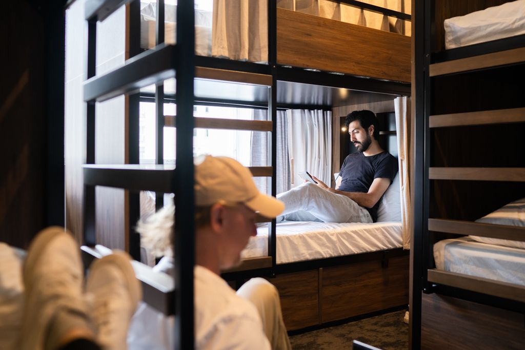 Two travelers relaxing on modern bunk beds in a stylish hostel dormitory room.