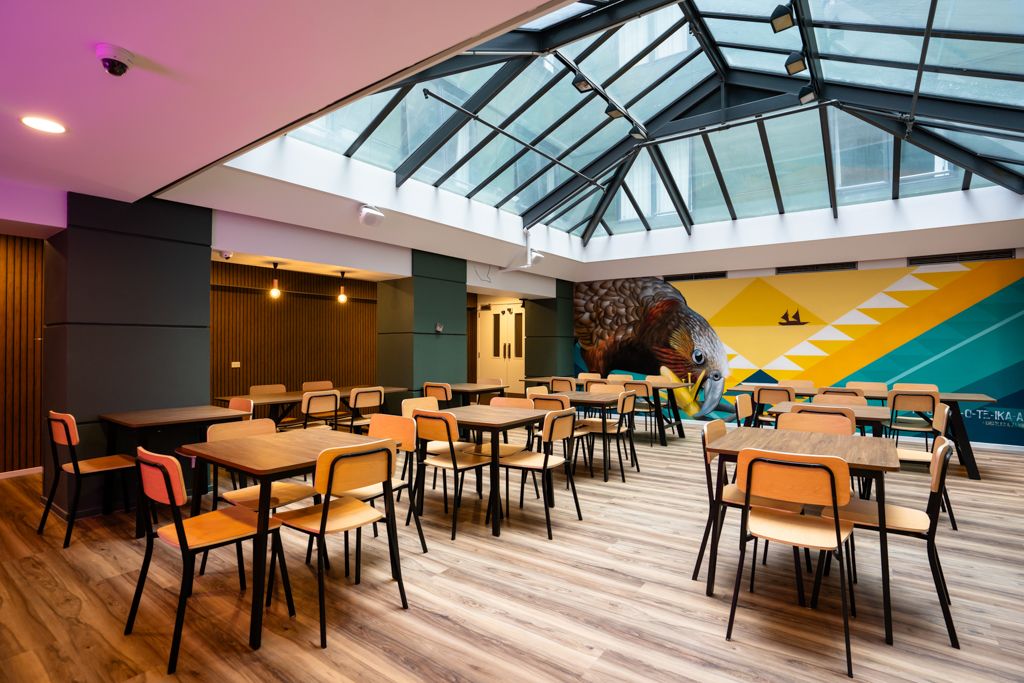 Bright dining area with skylight ceiling, colorful mural, and wooden tables and chairs.