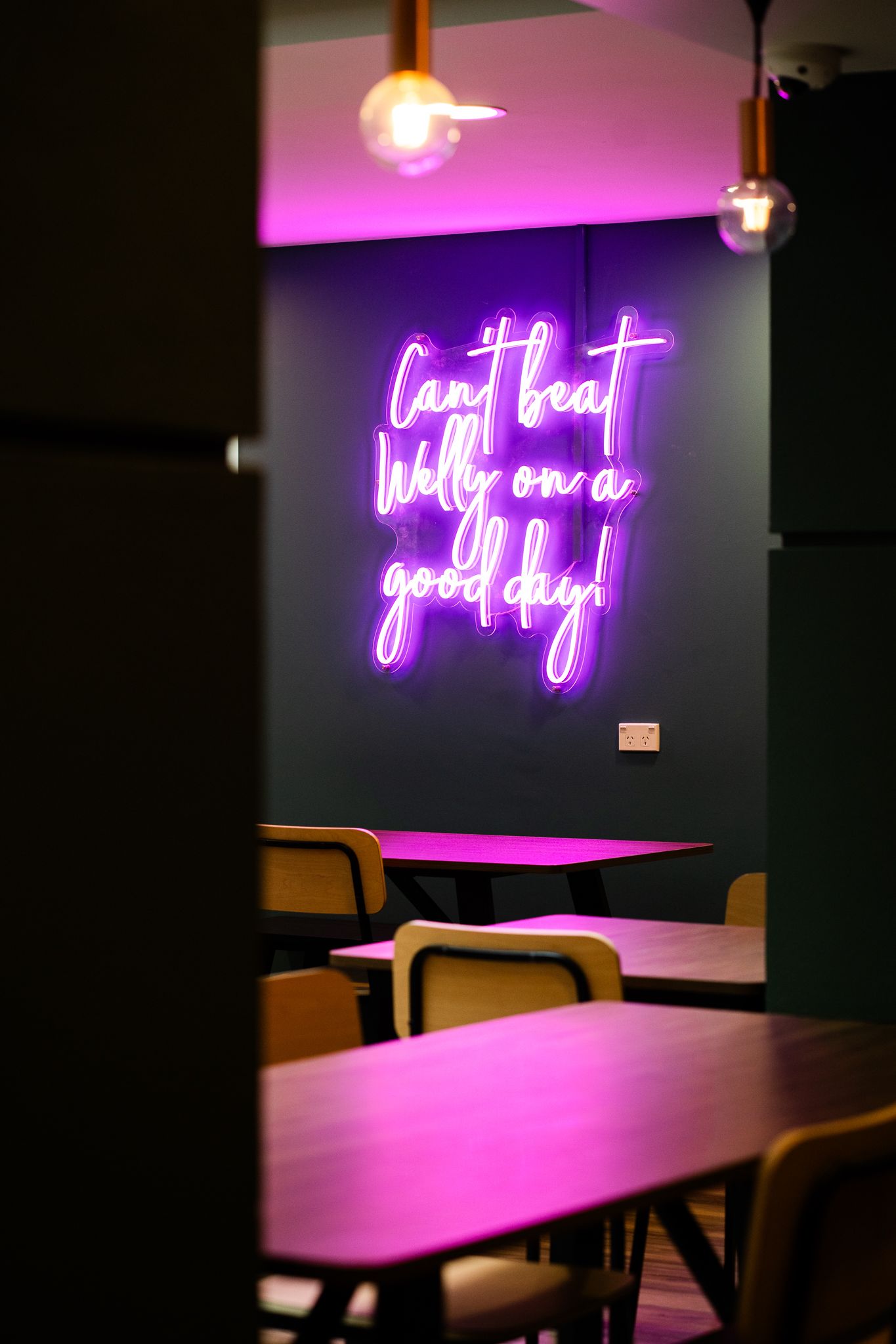Trendy restaurant interior with purple neon sign reading Can't beat Wally on a good day on dark wall.